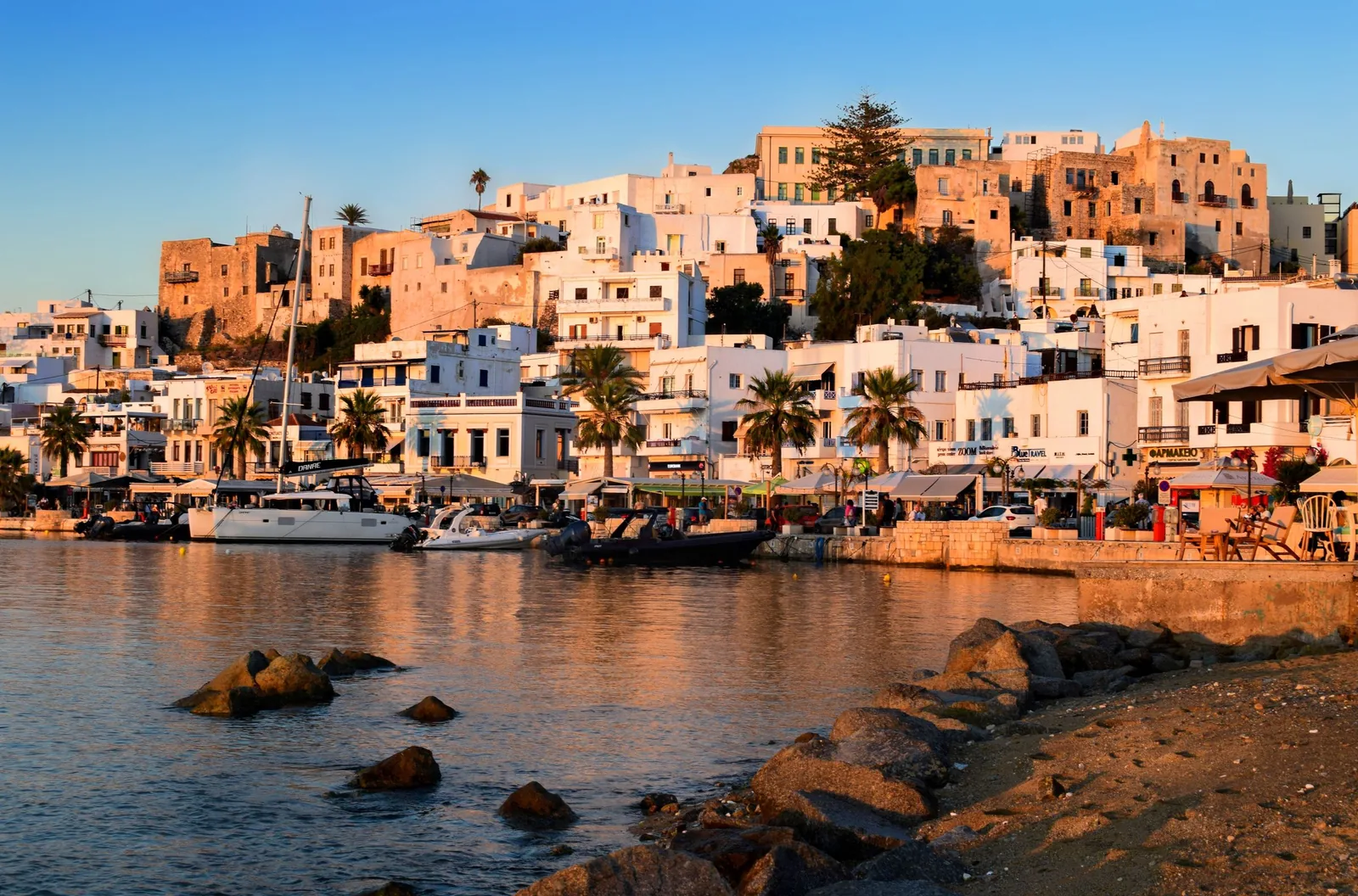 Naxos Town and its harbour at golden sunset, with terracotta-lit buildings rising above the water